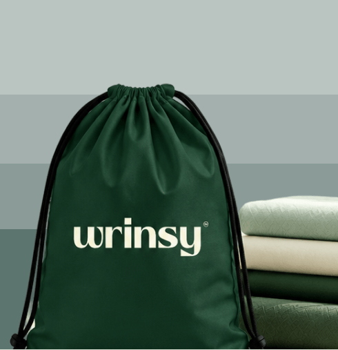 A green wrinsy drawstring laundry bag beside a stack of folded clothes