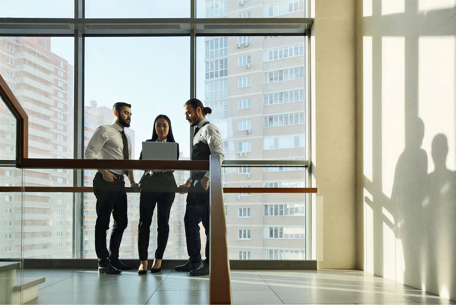Three colleagues reviewing a laptop by a floor-to-ceiling window
