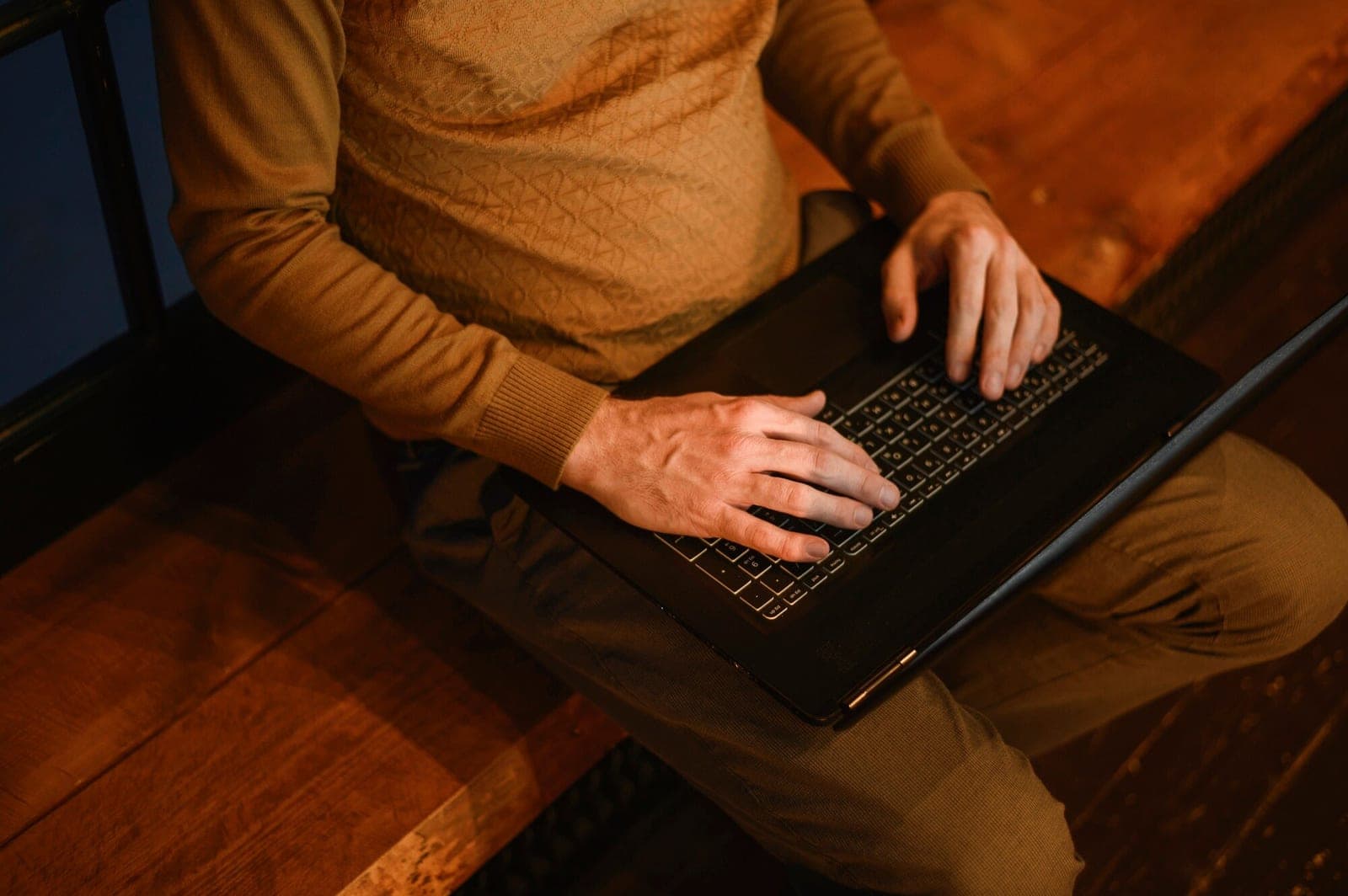 A person typing on a laptop in warm, low light